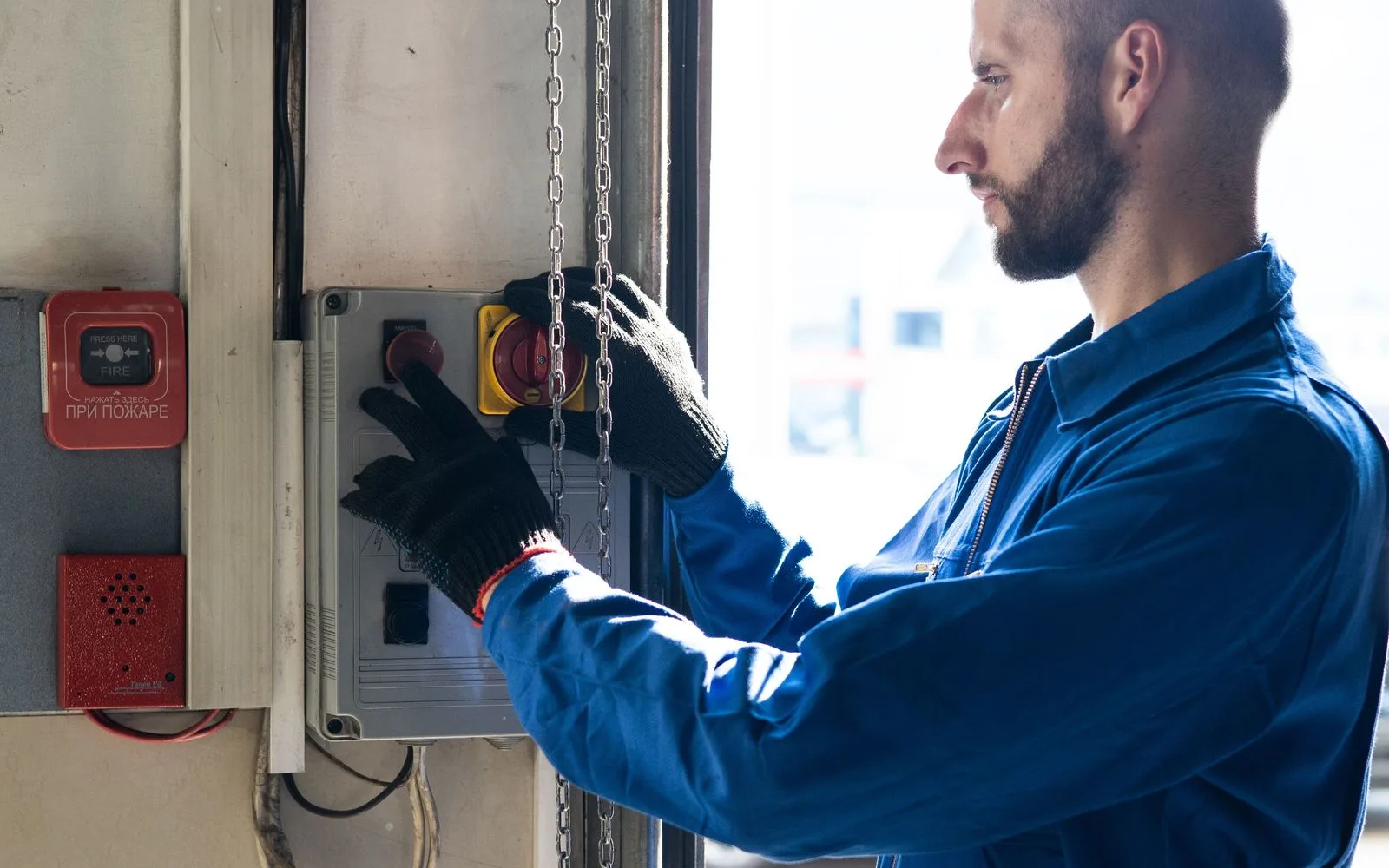 Hand mit Arbeitshandschuh an einem Bedienfeld in der Werkhalle