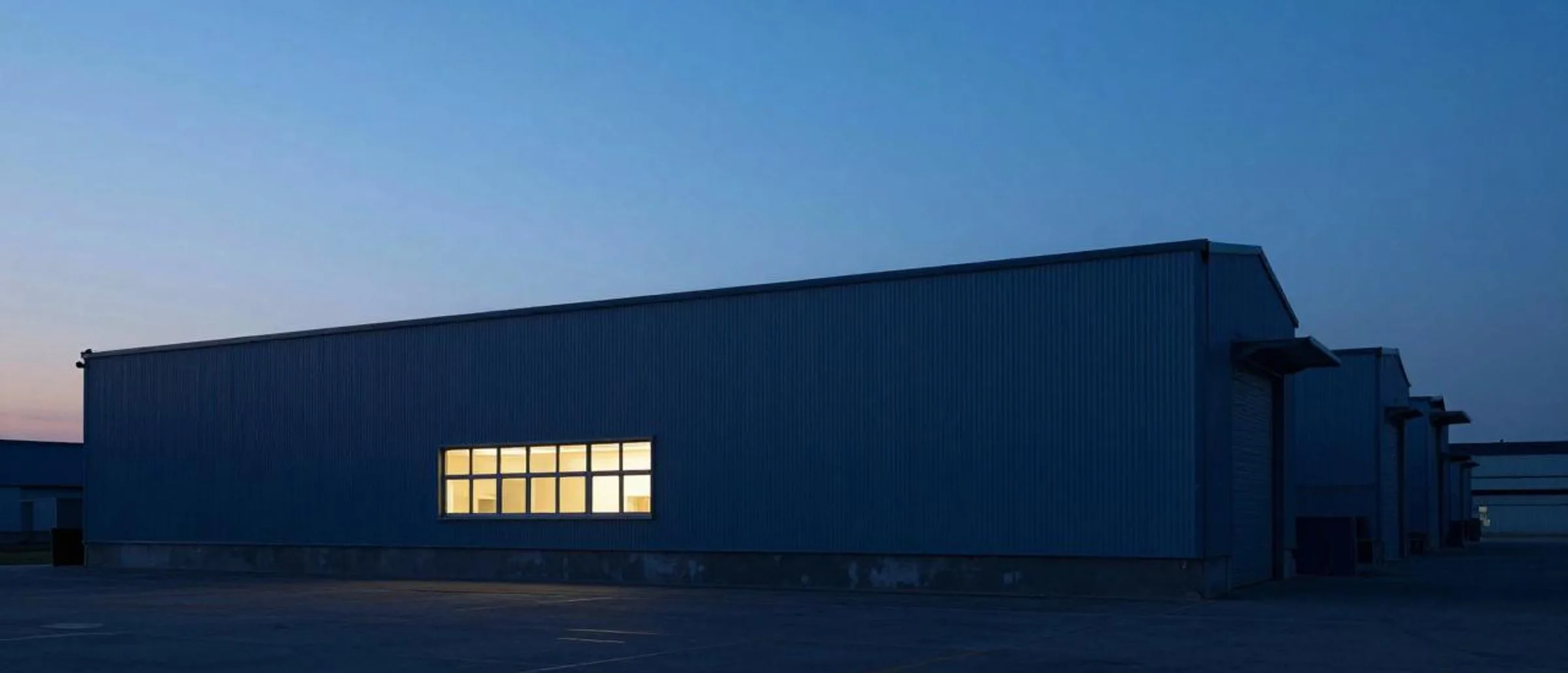 Industrial building at dusk with a single lit window